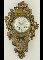 Cartelklok Louis XV, Frankrijk, ca. 1760.<BR/>
De klok is op de wijzerplaat gesigneerd 'Boussot � Paris'.<BR/><BR/>

Het 8-daags uurwerk heeft een ankergang. Met halfuurslagwerk op een bel.<BR/><BR/>

De rijk gestoken notenhouten kast is een ode op de kunsten.
Bovenop vindt men Bacchus, de god van de roes en de dronkenschap, maar ook van de inspiratie en de schone kunsten.
Linksboven de attributen van de schilders, het palet, de ezel en de penselen. Linksonder een portet van een portretschilder.
Rechtsboven de attributen van de schrijvers, hoorn des overvloeds, een boek, perkament en de muze.
Rechtsonder is de beeldhouwkunst weergegeven middels een hamer, beitels, liniaal en passer.
Onderop is de adelaar te zien, verbeelding van macht, schoonheid en onafhankelijkheid. Zittend op een mand met maretakken, de beschermer tegen ziekte en onheil.
