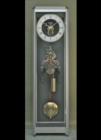 Uurwerk met 1-minuut remontoir. Klok wordt automatisch electrisch opgewonden. 1,98 x 0,55 x 0,40 mtr. 
Het uurwerk is een speciale uitvoering van een Ungerer of Schwilgue uit Strasbourg, ca. 1890, en een s.g. remontoir. Het uurwerk loopt feitelijk op een veer. Deze veer wordt elke minuut opnieuw opgewonden door het gewicht. De kracht op het Graham-gangsysteem zijn hierdoor constant (force constante). 
Het automatisch opwind-systeem is verborgen onder en klok achter de klokkast. het opwinden gebeurd elke 4 a 5 uur circa 20 seconden. 
De kast is van hoge kwaliteit geanodiseerd aluminium met 8 mm glas in de zijpanelen en een 6mm glazen deur. Het eveneens antieke wijzerwerk wordt aangedreven door het uurwerk aan de achterzijde van de klok. The elektronica werkt op 220 V.